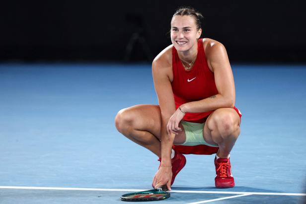 Aryna Sabalenka hockt lächelnd auf einem Tennisplatz.
