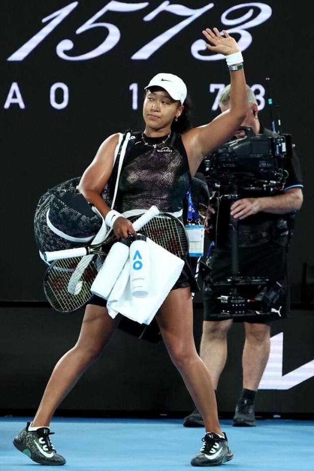 Naomi Osaka verlässt mit Tennisschlägern und einer Wasserflasche den Platz und winkt.