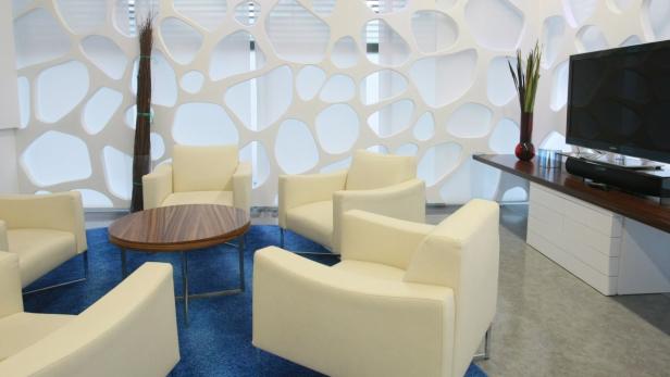 Ein Wartebereich mit cremefarbenen Sesseln und einem runden Tisch auf einem blauen Teppich.