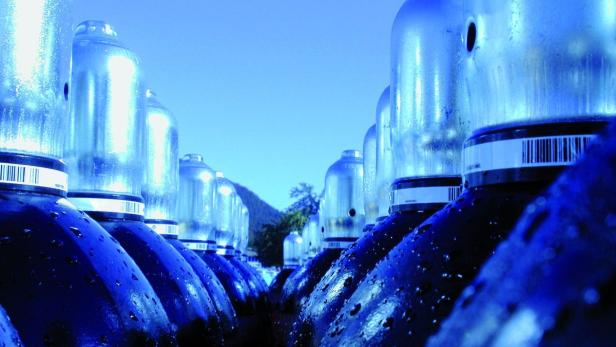 Eine Reihe blauer Gasflaschen vor einem bewaldeten Hügel.