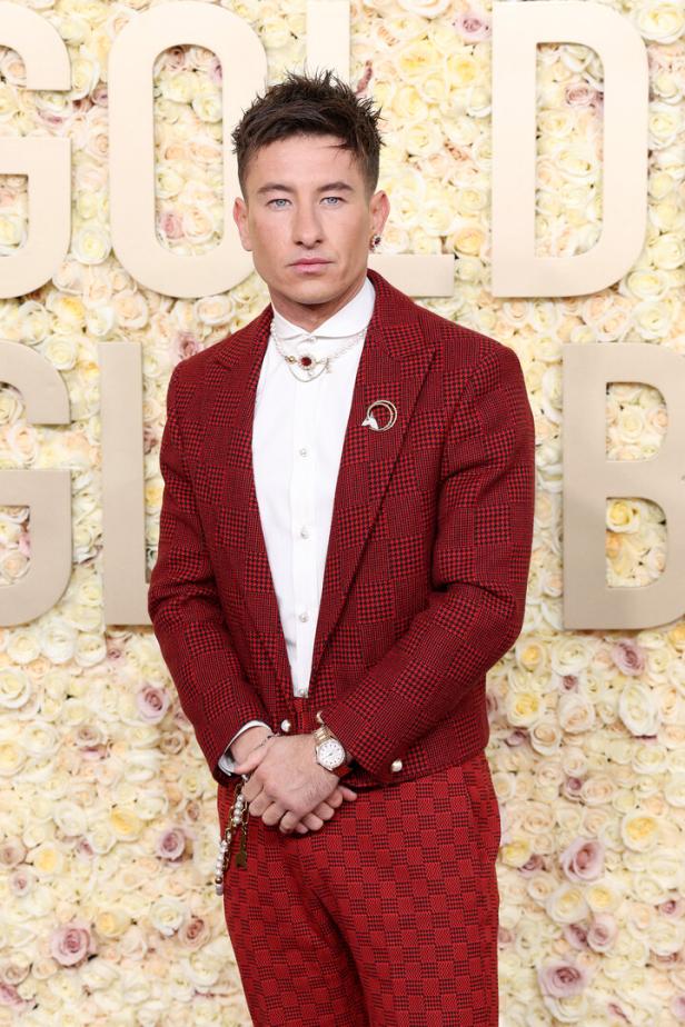 Barry Keoghan in einem rot karierten Anzug vor einer Wand aus Rosen.
