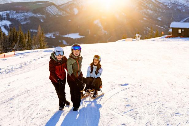Drei junge Frauen verbringen einen sonnigen Tag beim Rodeln im Schnee.