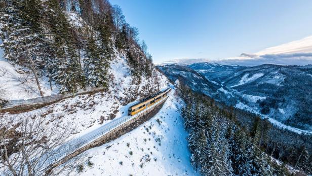 Ein gelber Zug fährt durch eine verschneite Berglandschaft.