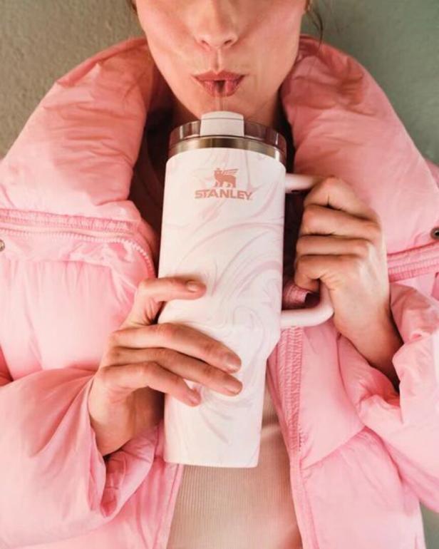 Eine Frau in einer rosa Jacke trinkt aus einem weißen Stanley-Becher.