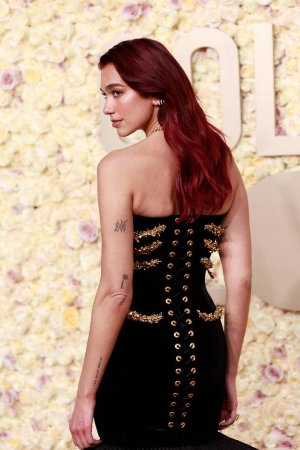 Dua Lipa in einem schwarzen, rückenfreien Kleid mit goldenen Akzenten.