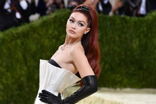 Gigi Hadid posiert in einem weißen Kleid und schwarzen Handschuhen.