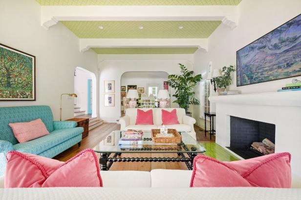 Ein helles Wohnzimmer mit einem türkisfarbenen und einem weißen Sofa mit rosa Kissen.