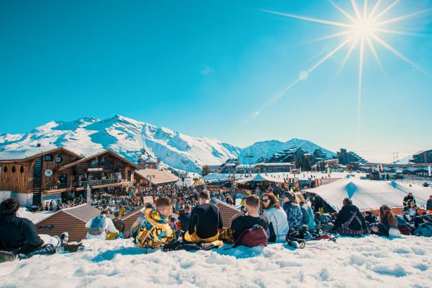 Eine Menschenmenge versammelt sich an einem sonnigen Tag in einem Skiort in den Bergen.