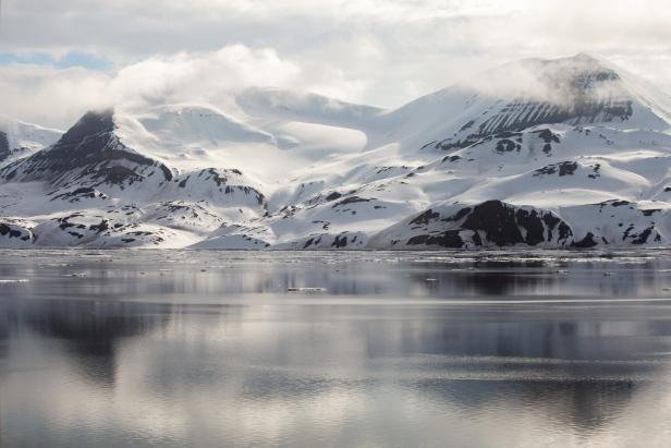 Schneebedeckte Berge spiegeln sich im ruhigen Wasser einer Bucht.