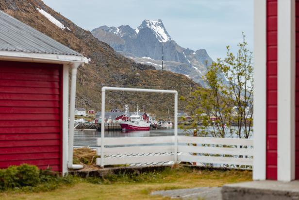 Ein rotes Fischerboot liegt in einem Hafen vor einer Bergkulisse in Norwegen.