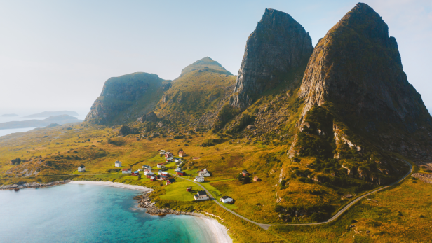 Blick auf ein kleines Dorf an einem Strand mit hohen Bergen im Hintergrund.
