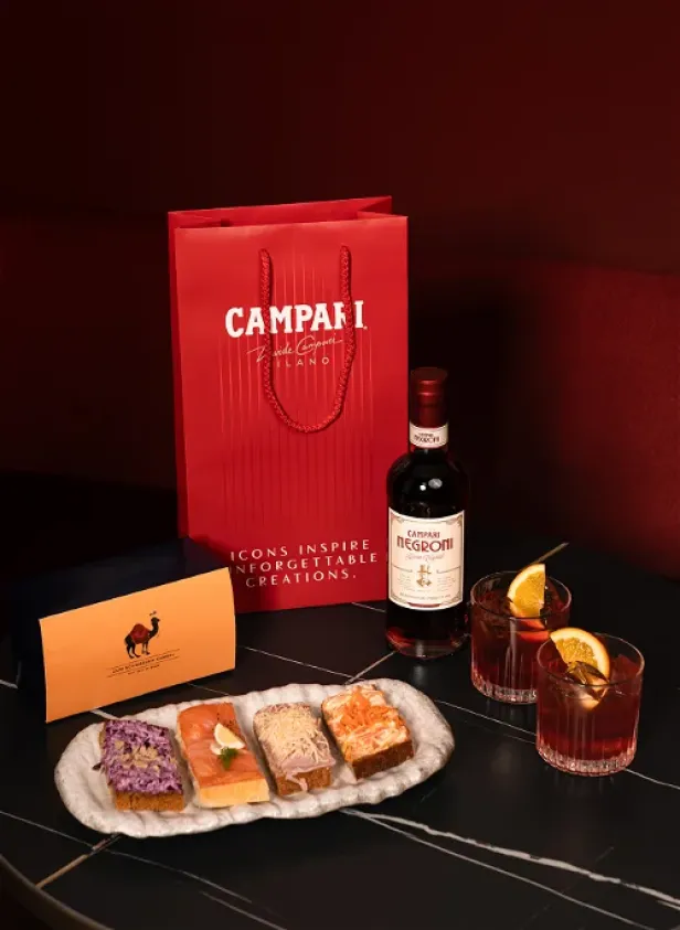 Ein Campari-Geschenkset mit Negroni-Flasche, Cocktails und belegten Broten.