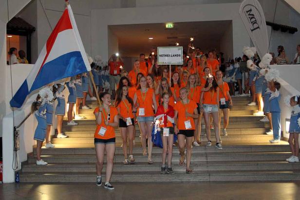 Eine Gruppe junger Frauen, angeführt von Fahnenträgern mit der niederländischen Flagge, geht eine Treppe hinunter.