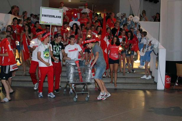 Eine Gruppe junger Leute in Schweizer Farben mit einem Schild „Switzerland“ und Wunderkerzen.