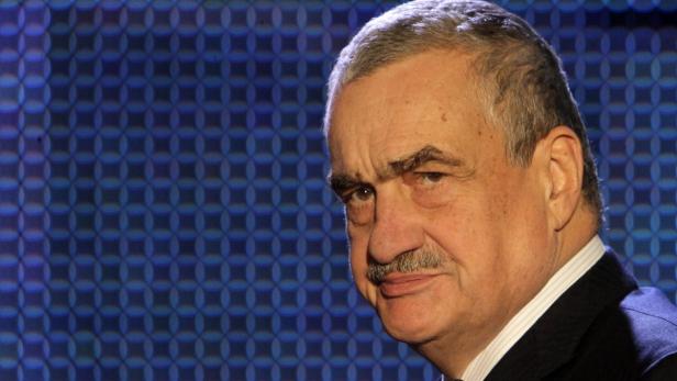 Ein Porträt eines älteren Mannes mit Schnurrbart vor einem blauen Hintergrund.