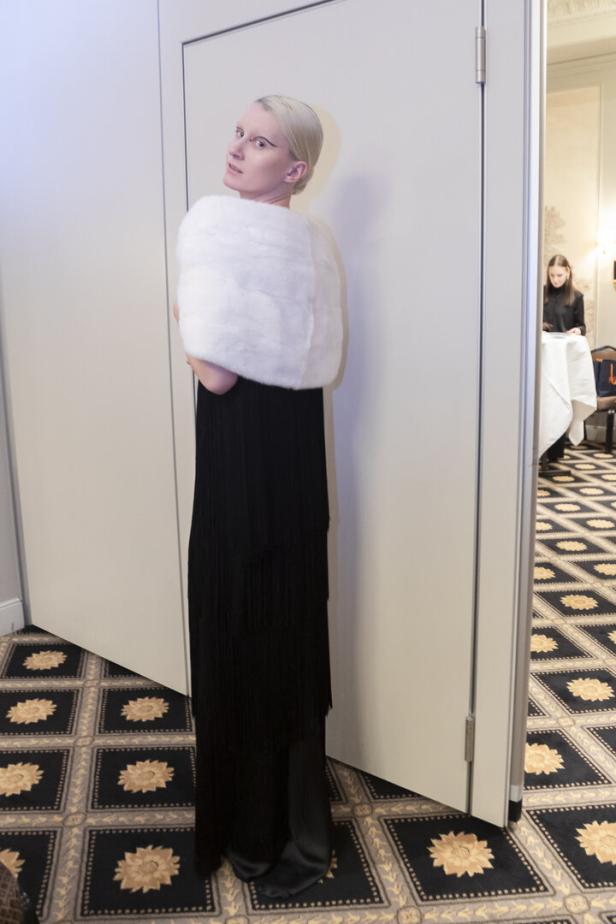 Eine Frau mit weißblondem Haar trägt ein schwarzes Kleid und eine weiße Stola.