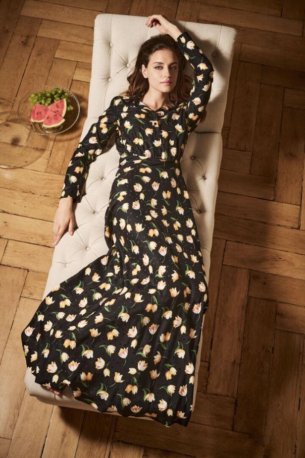 Eine Frau liegt in einem geblümten Kleid auf einer Ottomane.