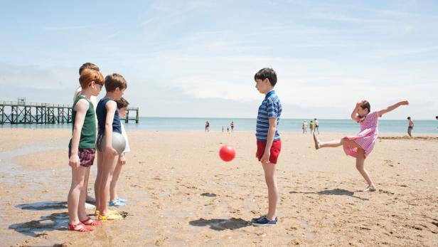 Eine Gruppe Kinder spielt mit einem roten Ball am Strand.