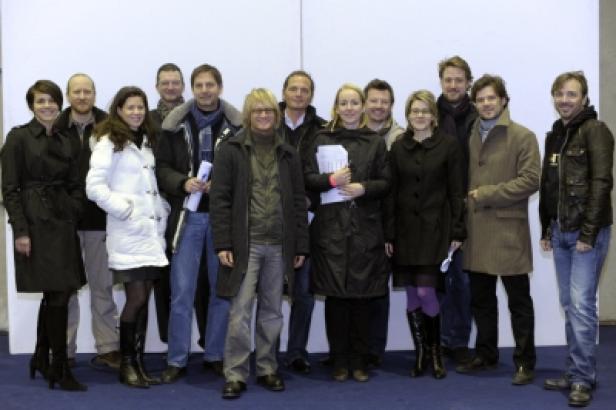 Eine Gruppe von etwa 14 Personen posiert für ein Gruppenfoto vor einem weißen Hintergrund.