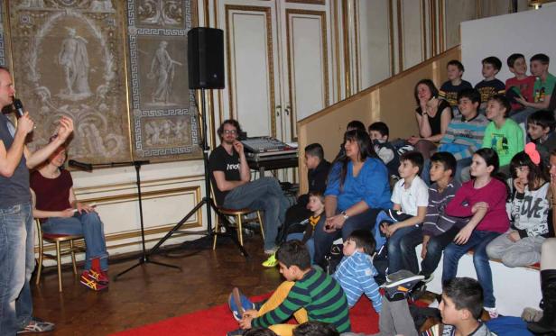 Eine Gruppe von Kindern und Erwachsenen sitzt auf einer Treppe und hört einer Präsentation zu.
