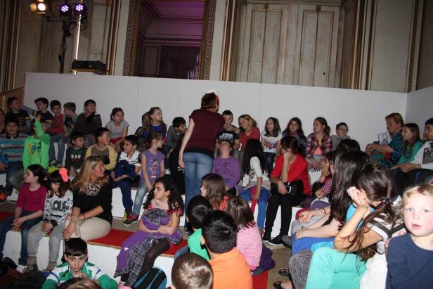 Eine Gruppe von Kindern sitzt auf einer Treppe in einem Raum.
