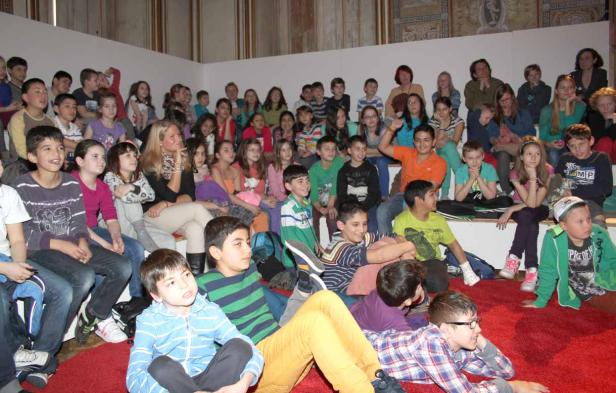Eine Gruppe von Kindern sitzt auf einer Treppe und schaut aufmerksam zu.
