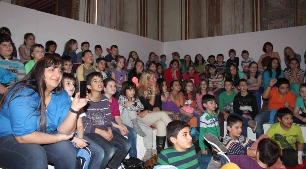 Eine Gruppe von Kindern sitzt auf einer Tribüne und schaut aufmerksam zu.