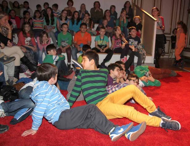 Eine Gruppe von Kindern sitzt auf dem Boden und auf Stufen und schaut zu.