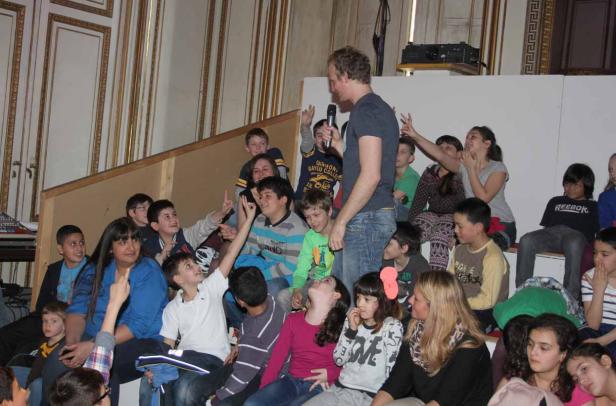 Ein Mann mit Mikrofon spricht vor einer Gruppe von Kindern.