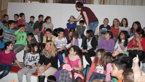 Eine Gruppe von Kindern sitzt auf einer Treppe, während eine Frau mit ihnen interagiert.