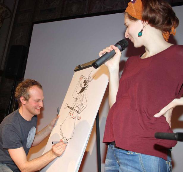 Ein Mann zeichnet eine Karikatur, während eine Frau mit einem Mikrofon daneben steht.