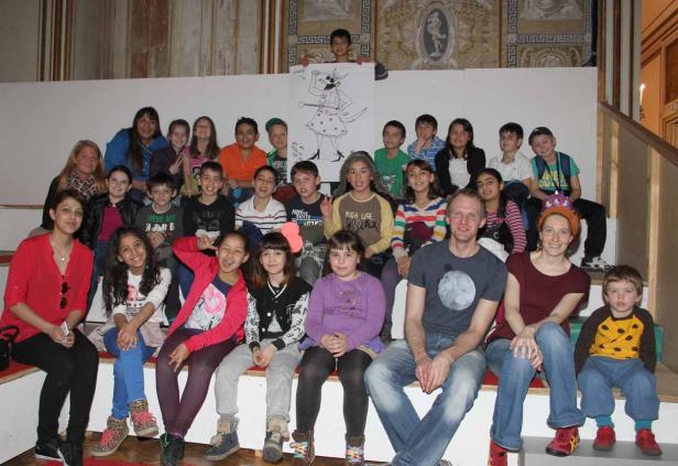 Eine Gruppe von Kindern und Erwachsenen posiert für ein Foto vor einem bemalten Hintergrund.