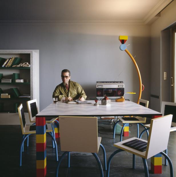 Karl Lagerfeld sitzt an einem bunten Tisch in einem Zimmer.