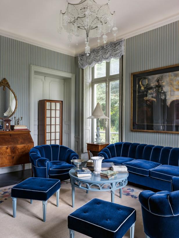 Ein Wohnzimmer mit blauen Samtmöbeln, gestreiften Tapeten und einem Kristalllüster.