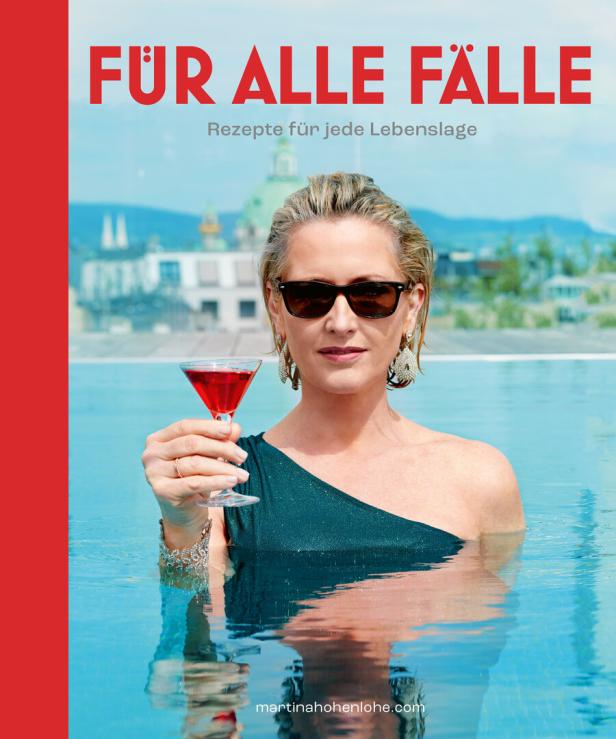 Eine Frau mit Sonnenbrille steht in einem Pool und hält ein rotes Getränk in der Hand.