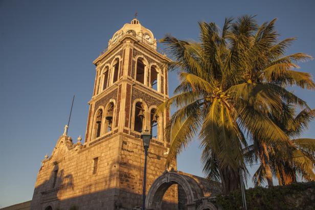 Die Kirche von Loreto, Baja California Sur, mit einem Glockenturm und Palmen im Vordergrund.