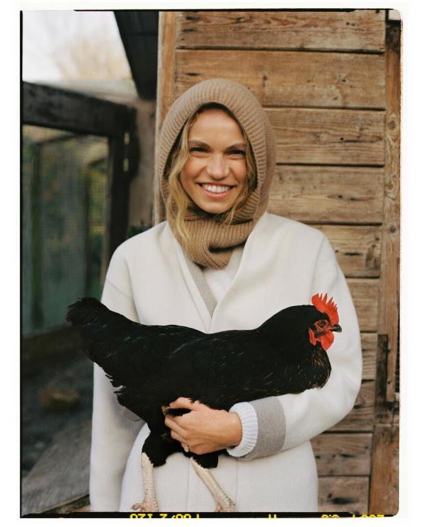 Eine lächelnde Frau hält ein schwarzes Huhn vor einer Holzwand.