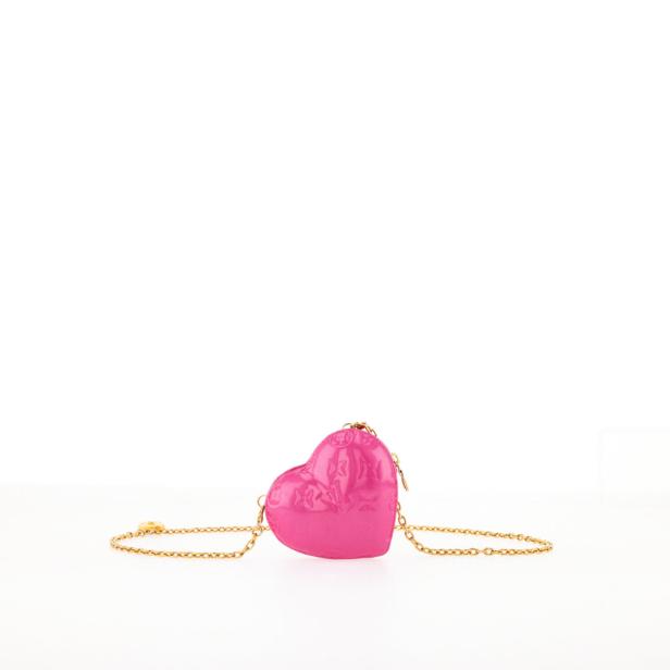 Eine pinkfarbene, herzförmige Handtasche mit goldener Kette auf einem weißen Hintergrund.