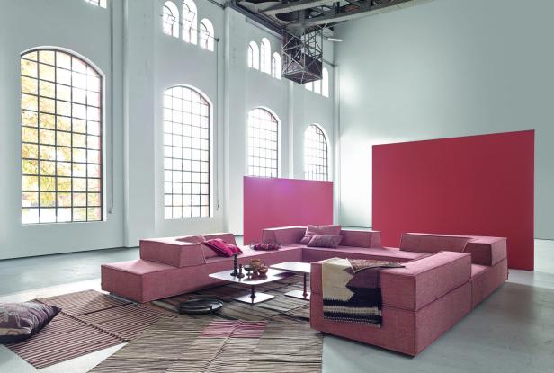 Ein großes, modulares Sofa in einem loftartigen Raum mit hohen Fenstern.