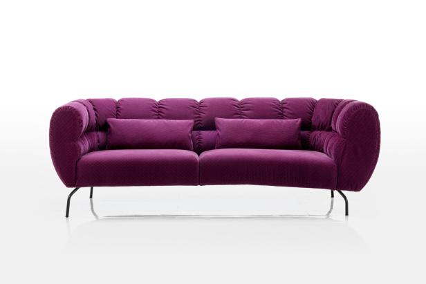 Ein lila Cordsofa mit zwei Kissen steht vor einem weißen Hintergrund.
