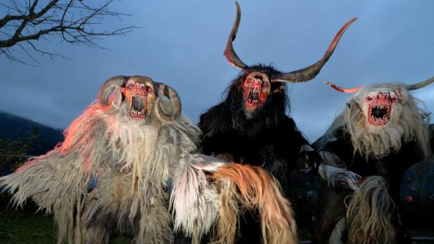 Drei furchterregende Krampusgestalten mit Hörnern und Fellkostümen stehen nebeneinander.