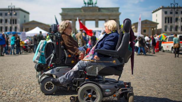 Zwei Frauen in Elektrorollstühlen unterhalten sich vor dem Brandenburger Tor.