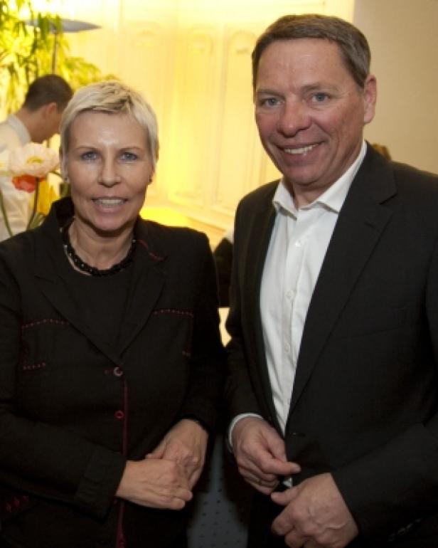 Eine Frau mit kurzem blonden Haar und ein Mann im Anzug lächeln in die Kamera.