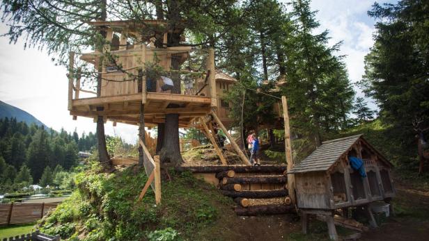 Ein großes Baumhaus mit mehreren Ebenen und Kindern, umgeben von Bäumen.