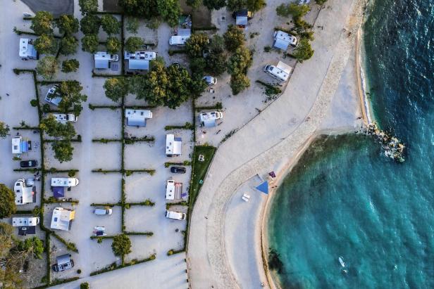 Luftaufnahme eines Campingplatzes am Strand mit Wohnwagen und türkisfarbenem Wasser.