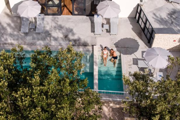 Ein Paar entspannt in einem türkisfarbenen Pool, umgeben von Bäumen und Liegestühlen.