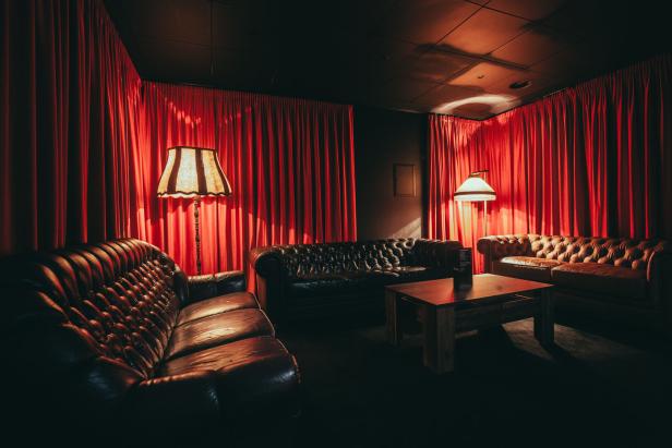 Ein dunkler Raum mit roten Vorhängen und drei Chesterfield-Sofas um einen Tisch.