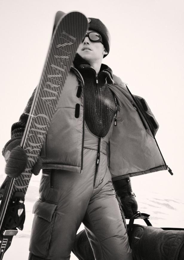 Ein Mann in Skikleidung und Brille trägt Skier über der Schulter.