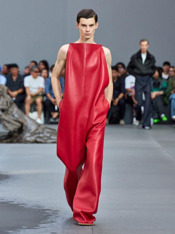 Ein Mann präsentiert auf einem Laufsteg einen roten, sackartigen Lederoverall.