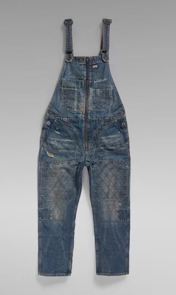 Eine blaue Jeans-Latzhose hängt vor einem grauen Hintergrund.